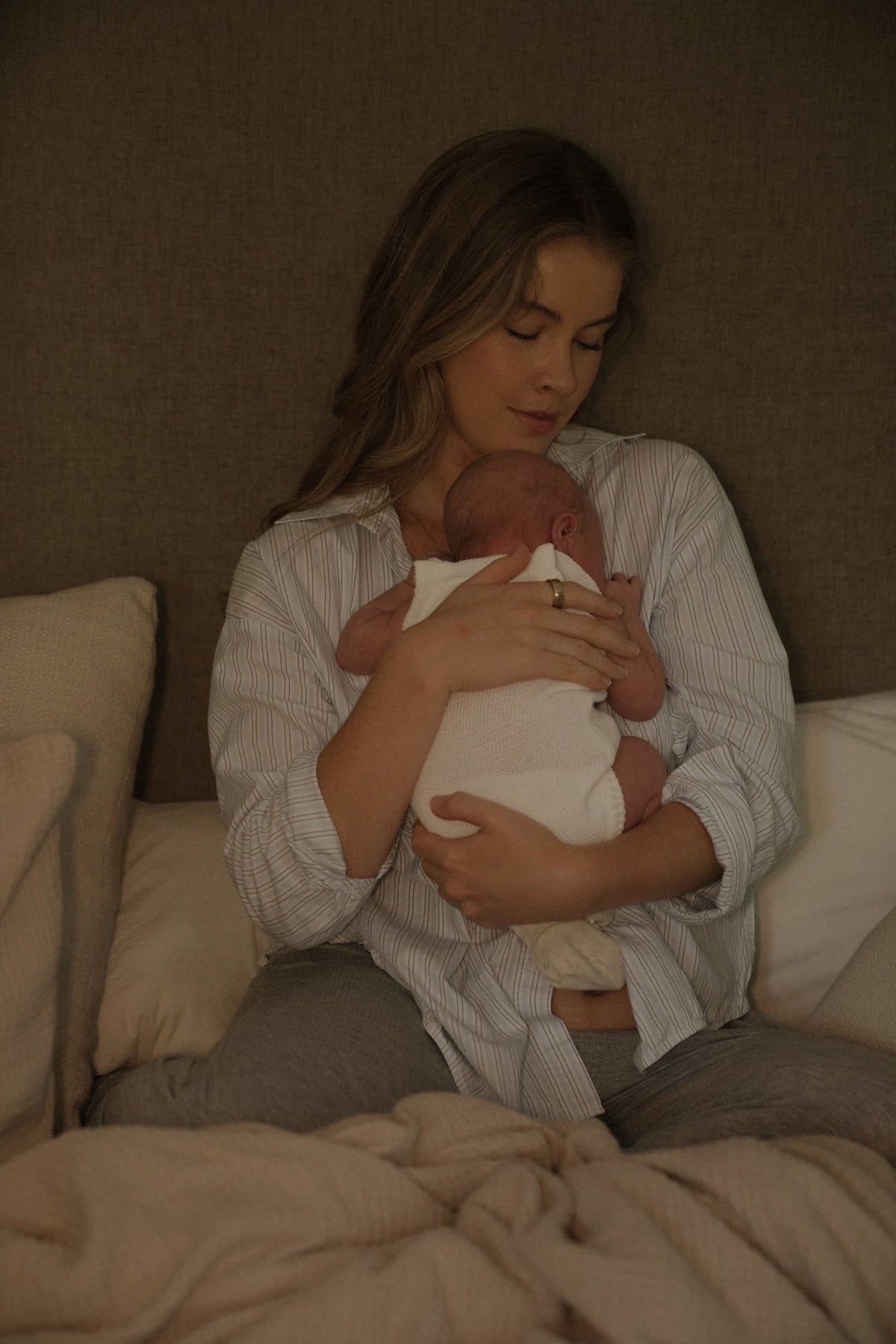 Monica Yates sitting in bed in a striped shirt, eyes closed, holding her newborn son against her chest